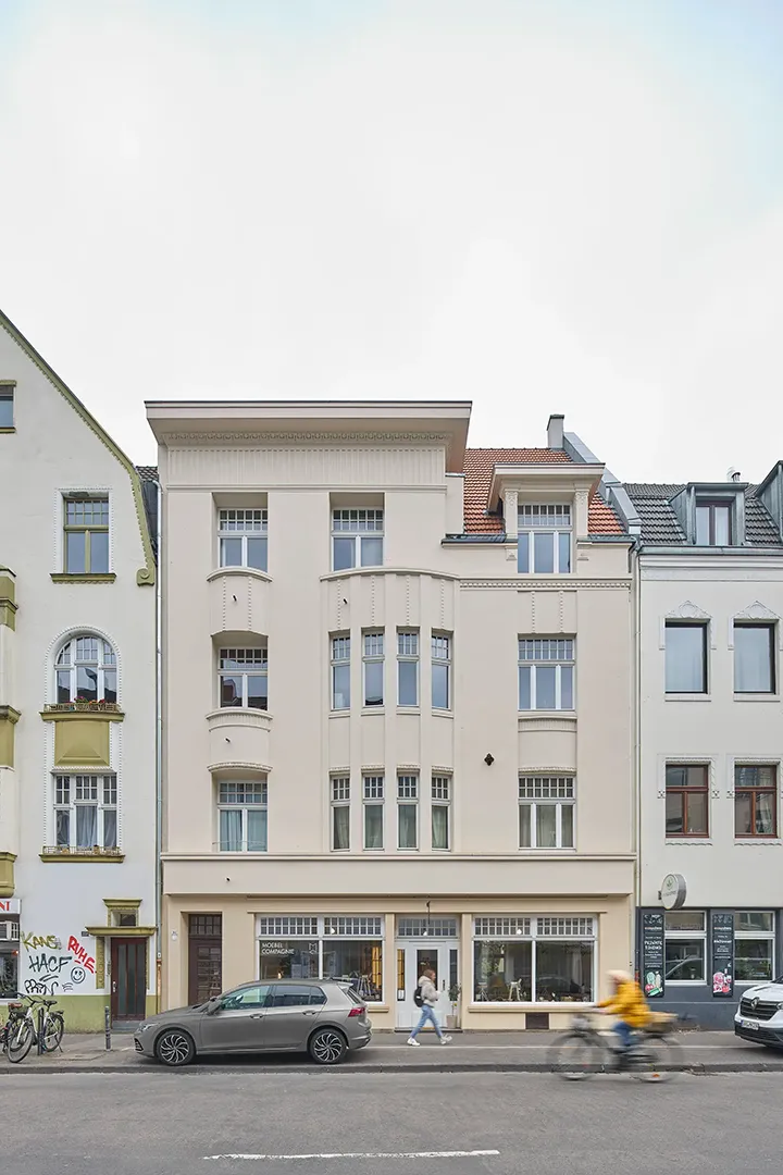 Straßenansicht eines sanierten viergeschossigen Altbaus mit gegliederter Stuckfassade, Erker über drei Geschosse, zurückgesetztem Dachgeschoss und Ladenlokal im Erdgeschoss.