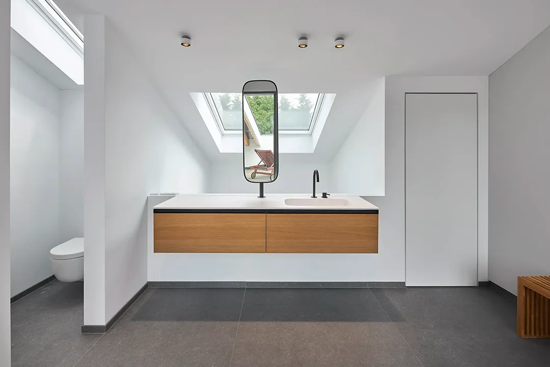 Achsensymmetrische Ansicht des wandhängenden Waschtischblocks unter der Dachschräge, Dachflächenfenster in der Mittelachse, links abgetrennter WC-Bereich, rechts flächenbündige Schiebetür.