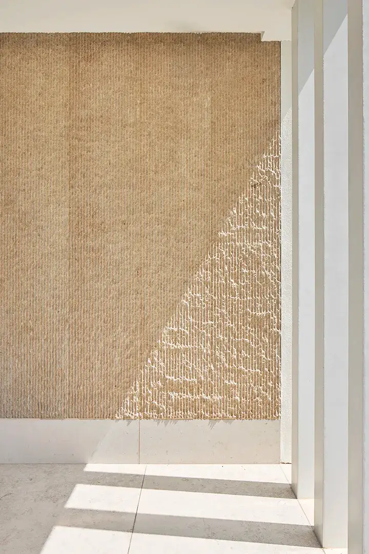 Detail der bossierten Natursteinwand im Eingangsbereich mit vertikaler Steinmetzstruktur, seitlich weiße Stützenscheiben, diagonal einfallendes Streiflicht auf Wand und Bodenplatten.