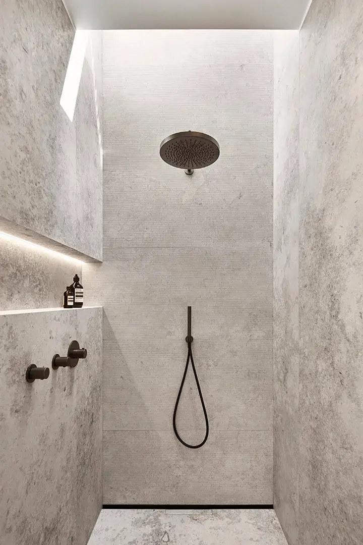Dusche mit umlaufender Natursteinverkleidung und fein geriffelter Rückwand, Deckenbrause und schwarze Armaturen, hinterleuchtete Wandnische und seitliches Lichtband.