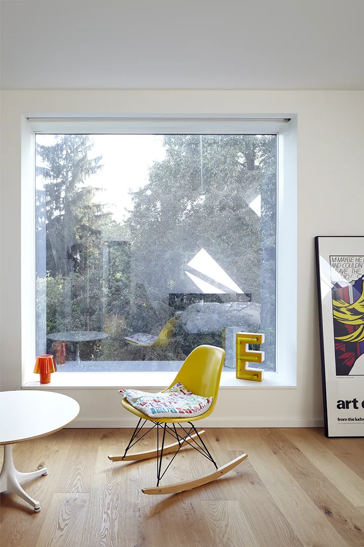 Großformatiges Festglasfenster mit tiefer Laibung als Sitzbank; das querformatige Glas rahmt den Blick in den begrünten Außenraum wie ein Bild.